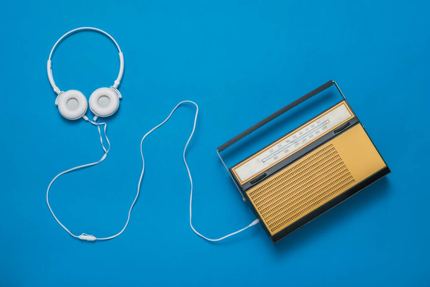 Valkoiset kuulokkeet, joissa on johto ja retro-radio sinisellä taustalla. Vintage-tekniikka. - Valokuva, kuva