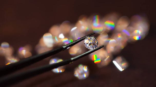 Діамант в пінцетах на темному тлі з групою алмазів м'яке фокусування
 - Фото, зображення