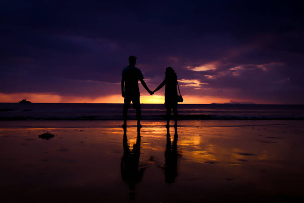 Silueta pár držet se za ruku a šťastný mladý pár láska na pláži při západu slunce - Fotografie, Obrázek