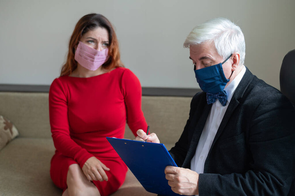 Male psychotherapist advises a female client in a medical mask. Moral support during the epidemic. Depressed woman on a visit to a psychologist. Hypochondria treatment. - Zdjęcie, obraz