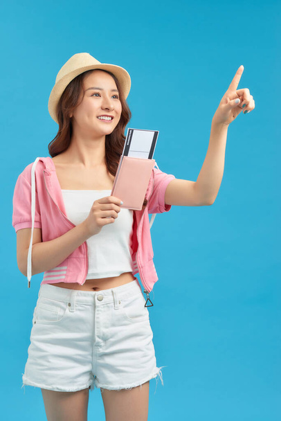 Młoda piękna azjatycka turystka na wakacjach trzymając paszport bardzo szczęśliwy dotykając ręką i palcem na bok - Zdjęcie, obraz