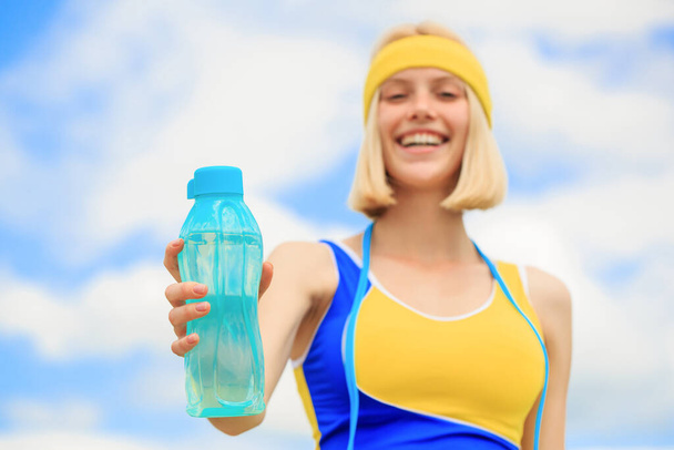 Gezond levensstijl concept. Een vrouw in sportkleding houdt een fles water vast. Jonge vrouw die water drinkt na het rennen. Sportmeisje drinkt water uit een fles op een hemelse achtergrond. Drinken tijdens de sport - Foto, afbeelding