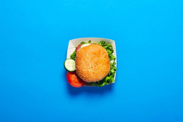 Hambúrguer fresco, pepino fatiado, tomate sobre um fundo azul brilhante. Deitado plano, vista superior
. - Foto, Imagem