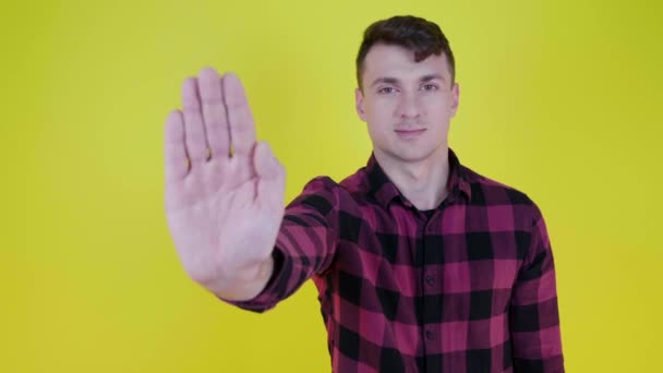 L'homme lève la main, montre la paume à la caméra et dit stop sur un fond jaune - Séquence, vidéo