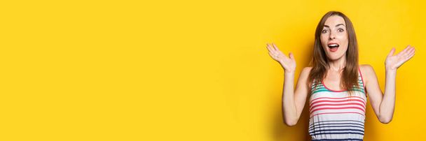 Jonge vrouw in een gestreepte zonnejurk verrast, verrast op een gele achtergrond. Banner. - Foto, afbeelding