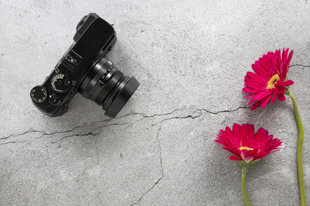 A modern DSLR camera and red gerbera flowers on cracked concrete background. Top view, flat lay design with copy space. - Photo, Image