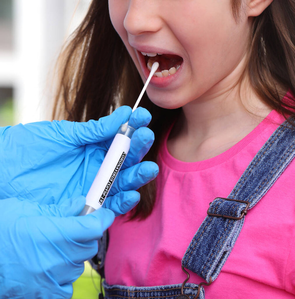 orvos latex kesztyű csinál egy tampont a lány a száját nyitott keresni a koronavírus - Fotó, kép