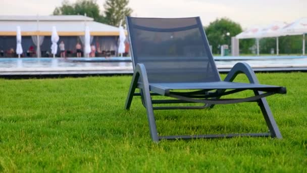 Una silla de cubierta vacía está de pie sobre la hierba contra el fondo de la piscina
 - Metraje, vídeo