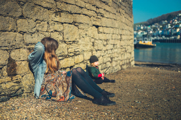 A young mother and her preschooler boy are relaxing on a pebble beach by a wall - Zdjęcie, obraz