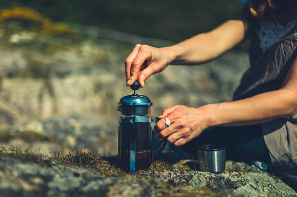 A young woman is using a french press to make coffee outdoors in nature - Foto, Imagem