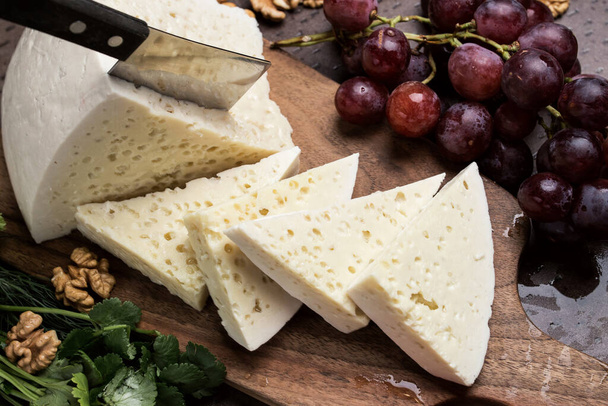 Slices of triangular cheese on a board. There are a lot of vegetables and grapes around. close-up top view. Georgian cuisine - Фото, зображення