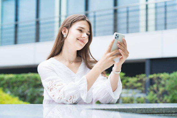 Uma mulher tocando e operando a tela de um smartphone ao ar livre
 - Foto, Imagem