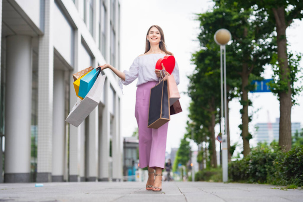 Μια νεαρή γυναίκα περπατά στην πόλη με πολλές τσάντες για ψώνια. - Φωτογραφία, εικόνα