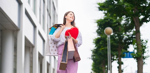 Een jonge vrouw die door de stad loopt met veel boodschappentassen - Foto, afbeelding