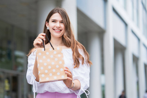 Mujer joven sosteniendo una bolsa de papel con regalos con una sonrisa
 - Foto, Imagen