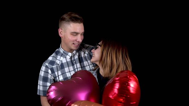 A young man gives a young woman heart-shaped balloons. The woman closed her eyes, and the man approached from behind. On a black background. Valentines Day is the day of all lovers. - Photo, Image