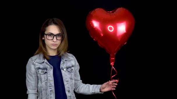 Een trieste vrouw staat met helium ballen op een zwarte achtergrond. Valentijnsdag is de dag van alle minnaars. - Foto, afbeelding