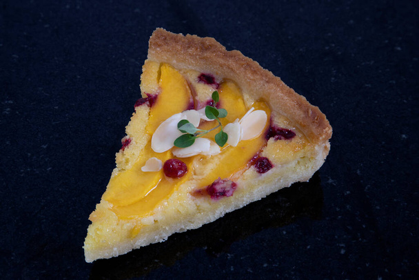  A single slice of fresh cranberry peach almond tart on a dark back granite kitchen background. - Photo, Image
