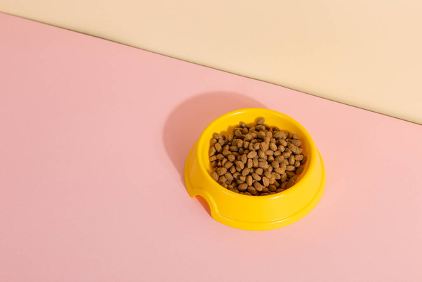 Κίτρινο μπολ με γατοτροφή σε χρωματιστό φόντο. έννοια της σωστής διατροφής των ζώων συντροφιάς. - Φωτογραφία, εικόνα