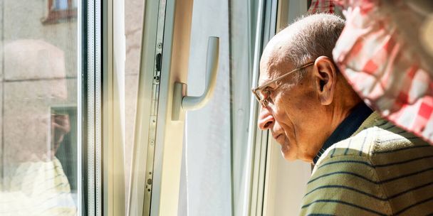 senior man in yellow pullover and glasses stands near window - Photo, image