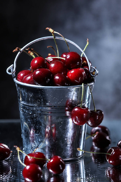 Red sweet cherries in a metal bucket on grey background. Summer taste. Fresh berries under the water drops - Foto, imagen