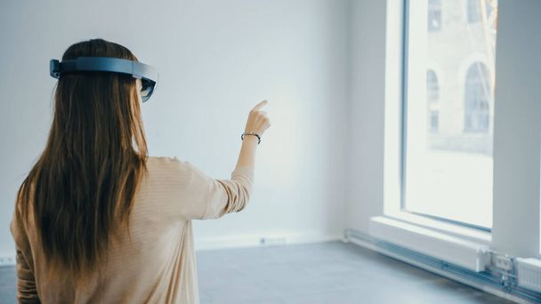Young Hipster Woman in Holographic Augmented Reality Glasses Standing in Empty Office and Map it. Sunlight Shines Through Big Windows. - Foto, Bild