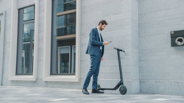 Businessman in a Suit is Activating an Electric Scooter with a Smartphone. Hes Scaning the QR Code. Modern Entrepreneur Uses Contemporary Ecological Transport to Go on an Office Meeting. - Photo, image