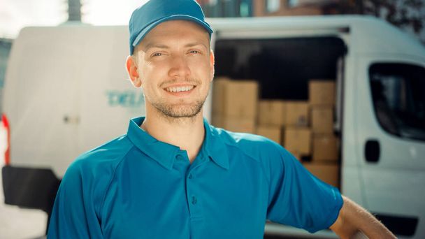 Portrait of Handsome Delivery Man Holds Cardboard Box Package Standing in Modern Stylish Business District with Delivery Van in Background. Smiling Courier On Way to Deliver Postal Parcel to Client - Fotó, kép