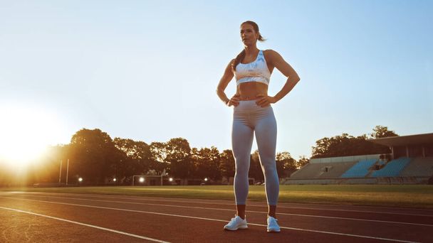 Beautiful Fitness Woman in Light Blue Athletic Top and Leggings is Catching Her Breath and Posing in a Stadium. She was Training on a Warm Summer Afternoon and Doing Her Routine Workout. - Foto, imagen