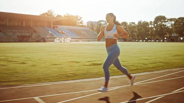 Beautiful Fitness Girl in Light Blue Athletic Top and Leggings Jogging in the Stadium. She is Running on a Warm Summer Afternoon. Athlete Doing Her Routine Sports Practice on a Track. - Φωτογραφία, εικόνα