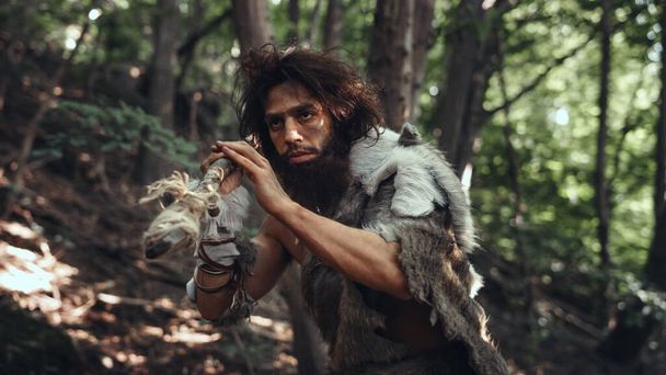 Portrait of Primeval Caveman Wearing Animal Skin and Fur Hunting with a Stone Tipped Spear in the Prehistoric Forest. Prehistoric Neanderthal Hunter Scavenging with Primitive Tools in the Jungle - Fotografie, Obrázek