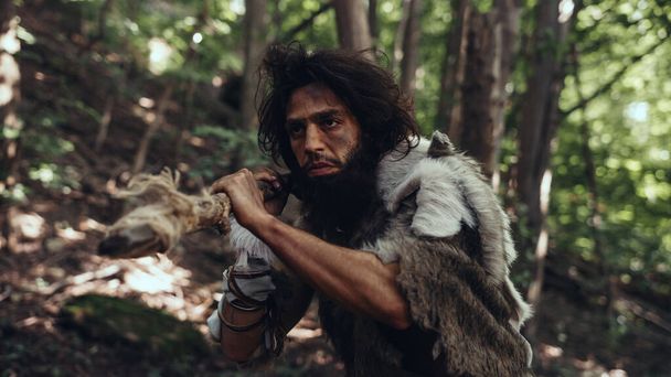 Portrait of Primeval Caveman Wearing Animal Skin and Fur Hunting with a Stone Tipped Spear in the Prehistoric Forest. Prehistoric Neanderthal Hunter Scavenging with Primitive Tools in the Jungle - Φωτογραφία, εικόνα