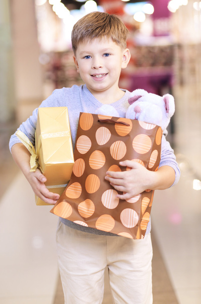 Lapsen hallussa paperipussi ja lahjapakkaus
 - Valokuva, kuva