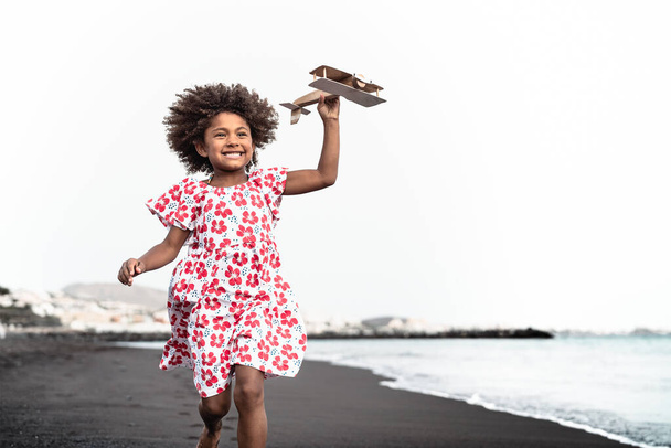 Afro dziecko bawiące się drewnianym samolotem zabawki na plaży - Little kid having fun during summer holidays - Koncepcja dzieciństwa i podróży wakacje - Zdjęcie, obraz