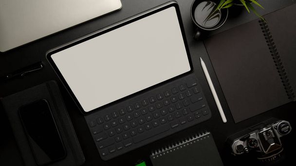 Widok z góry tabletu z klawiaturą na ciemnym, luksusowym biurku z wyposażeniem biurowym, aparatem fotograficznym i dekoracją - Zdjęcie, obraz