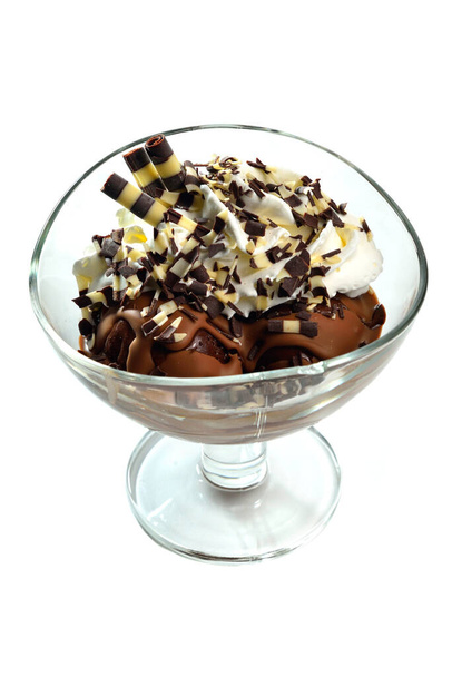 Sorvete de chocolate sundae com tubules doces, chantilly e flocos de chocolate em copo de vidro sobre fundo branco
 - Foto, Imagem