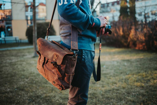 A shallow focus shot of a man with a camera and brown leather bag - Fotoğraf, Görsel