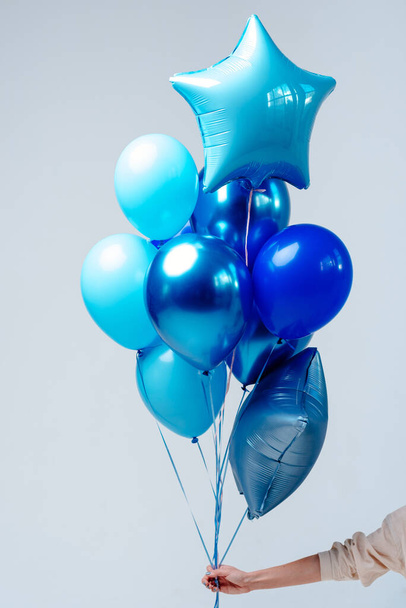 Composition of dark blue, blue, transparent helium balloons and two sapphirine star in the hand of a woman on a white background. - Фото, зображення