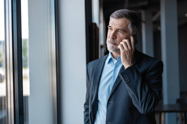 Senior business man talk on mobile phone at modern bright office interior. - Фото, изображение