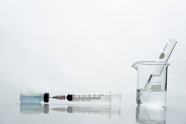 стеклянный стакан и пробирка с препаратом в шприц инъекции в медицинской лаборатории здоровья
 - Фото, изображение