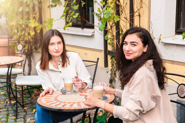 Two women drink coffee in cafe and pose for camera - Фото, зображення