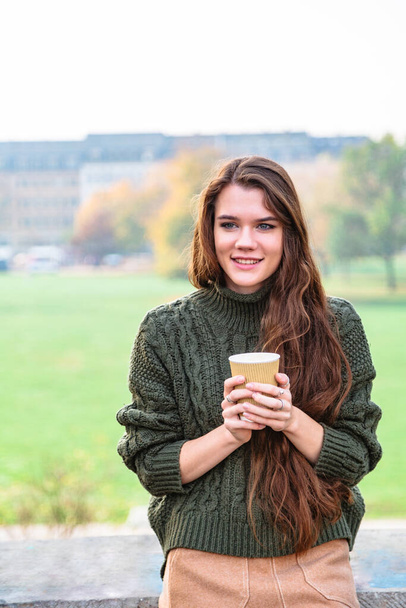 Smiling girl with cup of coffee sits on fence - Foto, Imagen