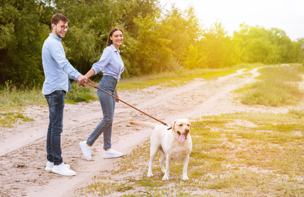 Cute couple and retriever walking in countryside - Photo, Image
