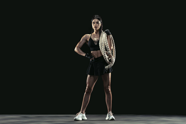 Kaunis nuori naisurheilija harjoittelee mustalla studiotaustalla, täyspitkä muotokuva - Valokuva, kuva