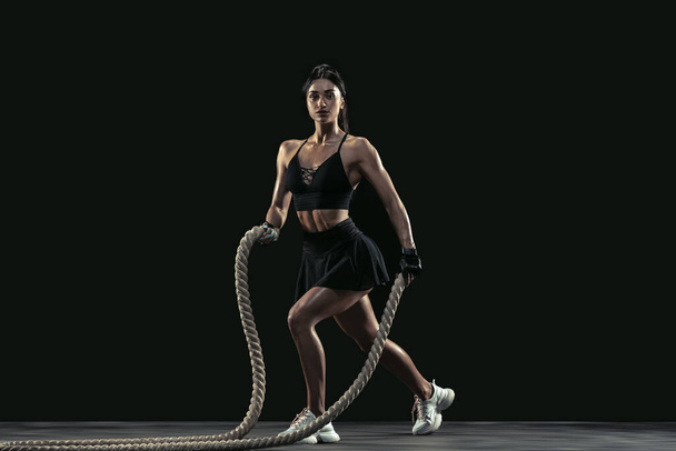 Beautiful young female athlete practicing on black studio background, full length portrait - Фото, изображение