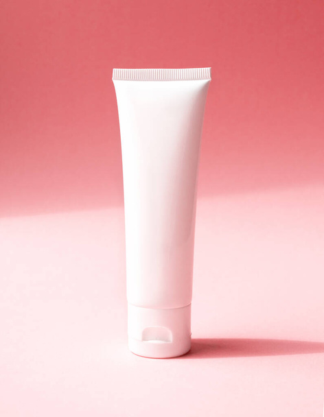 Close-up mockup üres fehér műanyag cső kozmetikai termék, elölnézet. Tartály kézkrém, hidratáló testápoló krém, arc tisztító vagy sampon rózsaszín alapon átlós árnyalatú háttér - Fotó, kép