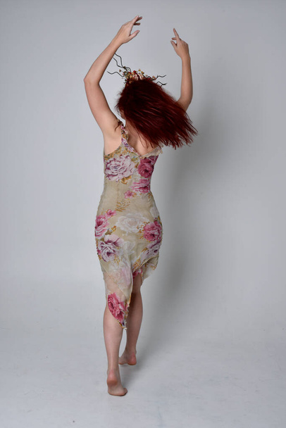 teljes hosszúságú portré vörös hajú lányról virágos ruhában és fejdísszel. álló póz szürke stúdió háttér. - Fotó, kép