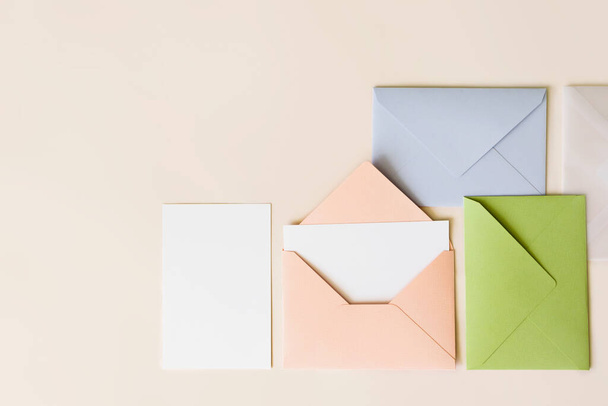 ピンクの封筒の中のモックアップの空白の手紙、空の白い紙とベージュの背景にカラフルな閉じた封筒、トップビュー。コピースペース付きグリーティングカードコンセプト。ユニバーサル招待テンプレート - 写真・画像