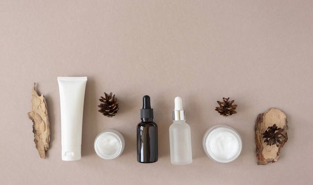Set for skin and body care beauty products and pine bark and cone on beige background. Mockup beauty treatment container flat lay, above. Plastic tube, glass jars and glass bottles with pipette - Photo, Image