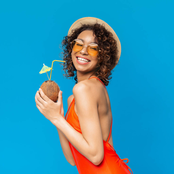 Счастливая черная девушка в купальниках наслаждается кокосовым коктейлем и улыбается в камеру
 - Фото, изображение